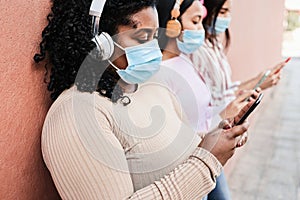 Young multiracial friends wearing protective masks while using mobile phone outdoors - Focus on right hand