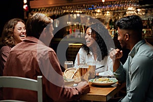 Young multiracial group of friends in casual clothing laughing around table with food and drinks