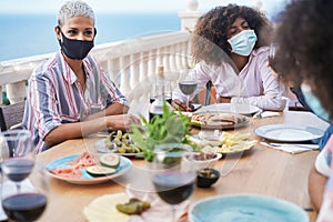 Young multiracial group of friends having dinner and wearing protective masks - Focus on african girl