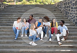 Young multiracial group of friends using mobile smartphone sitting on stairs out of college