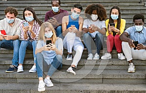 Young multiracial group of friends using mobile smartphone while wearing face mask during covid19