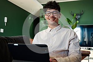 Young multiracial man in shirt smiling while using digital tablet with wireless headphones at home