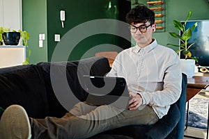 Young multiracial man using digital tablet with wireless headphones on sofa with feet up at home