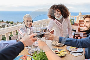 Young multiracial people cheering with wine and eating with masks under chins at patio restaurant - Focus on african woman face