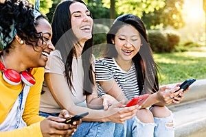 Young multiracial woman friends having fun using mobile phones in the street