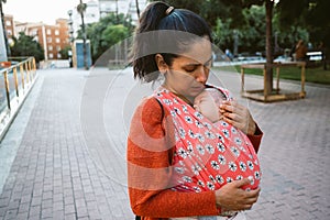 Young mum babywearing in the city. baby in wrap carrier during porting. Modern and natural motherhood outdoors