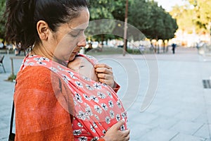 Young mum babywearing in the city. baby in wrap carrier during porting. Modern and natural motherhood outdoors