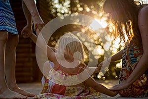 Young mum with blonde daughter girls smiling doing ring around the rosie . Warm sunset light. Family summer travel