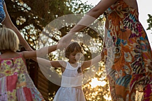 Young mum with blonde daughter girls smiling doing ring around the rosie . Warm sunset light. Family summer travel