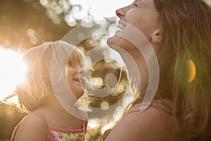 Young mum holding his blonde daughter girl on his arms and laughing or smiling. Warm sunset light. Family summer travel