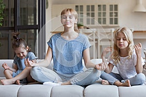 Young mum and little daughter meditate on home couch