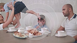 Young mum playing with her baby boy while dad talking to his son sitting at the tea table