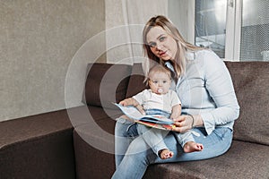 Young mum is reading a book with her cute son sitting on the couch