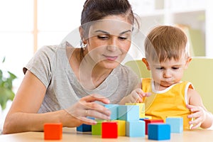 Young mummy and her kid play with cubes toys in nursery