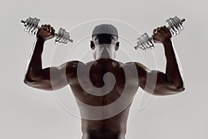 Young muscular african american man lifting weights, standing isolated over grey background. Sports, workout