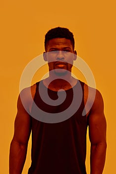 Young muscular african american man looking at camera, posing isolated over orange background. Sports, workout