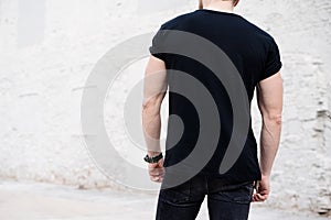 Young muscular bearded man wearing black tshirt and jeans posing in center of modern city. Empty concrete wall on the