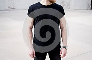 Young muscular bearded man wearing black tshirt and jeans posing in center of modern city. Empty concrete wall on the