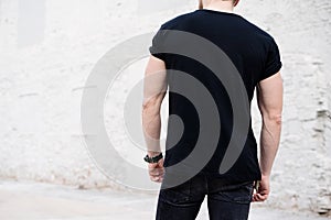 Young muscular bearded man wearing black tshirt and jeans posing in center of modern city. Empty concrete wall on the photo