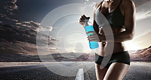 Young muscular build woman silhouette drinking water of bottle.