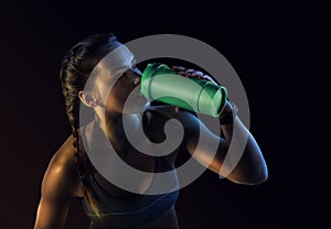 Young muscular build woman silhouette drinking water of bottle.