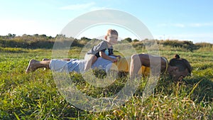 Young muscular father doing push ups with his little son on his back. Athletic man doing push-ups at green grass with