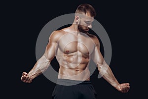 Young muscular and fit young bodybuilder fitness male model posing and demonstrating his muscles isolated on black