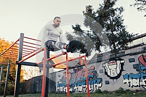 Young muscular good looking man working out on his abs using the horizontal ladder and parallel bars station