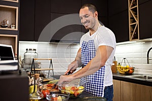 Young muscular guy with apron preparing to cook a delicious meal from confinements of his kitchen, cooking from home