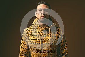 Young muscular Hispanic man wearing hoodie against brown background