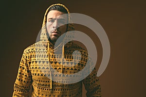 Young muscular Hispanic man wearing hoodie against brown background