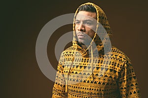 Young muscular Hispanic man wearing hoodie against brown background