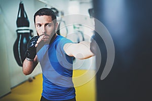 Young muscular kickboxing fighter practicing kicks with punching bag.Boxing on blurred background.Concept of a healthy