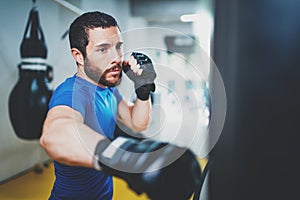 Young muscular kickboxing fighter practicing kicks with punching bag.Kick boxer boxing as exercise for the fight.Boxer