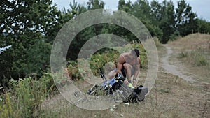 A young muscular man in blue shorts squats next to his bike and backpack and ties up his sneakers before training in