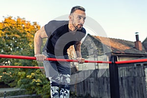 Young muscular man doing calisthenics outside lifting himself above the bar, street gymnastics