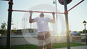 Young muscular man doing pull-ups on horizontal bar. On workout area near house