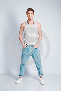 Young muscular man in a light T-shirt and jeans on a white background. Copy, empty space for text