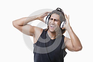 Young muscular man listening music through headphones over white background