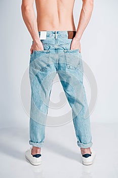 Young muscular man with a naked torso dressed in blue jeans on a white background. Copy, empty space for text