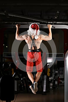 Young muscular man in Santa costume training gym