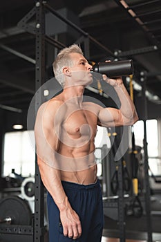 Young muscular man showing his perfect body. Man drinking from a cocktail shaker with the protein. Toned image