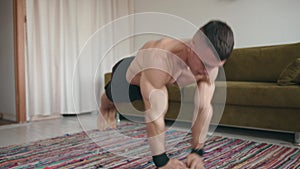 Young muscular man training at home and doing push-ups in exercise plank by moving his arms on the mat