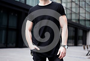 Young muscular man wearing black tshirt and jeans posing in center of modern city. Blurred background. Hotizontal mockup