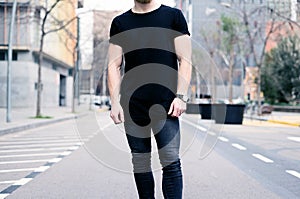 Young muscular man wearing black tshirt and jeans posing on the street of the modern city. Blurred background photo