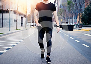 Young muscular man wearing black tshirt and jeans walking on the streets of the modern city. Blurred background