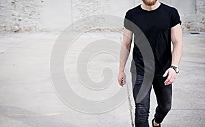 Young muscular man wearing black tshirt and jeans walking on the urban district. Blurred background. Hotizontal mockup.