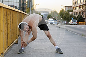 Young muscular runner for a stretching exercise on a bridge