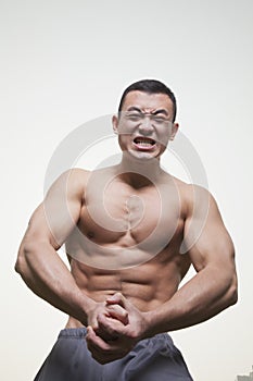 Young, muscular, shirtless man growling and flexing his muscles, studio shot