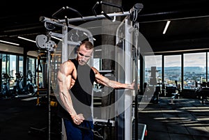 Young muscular sweaty fit bodybuilder man doing triceps workout training in the gym on cable machine for big arms muscles